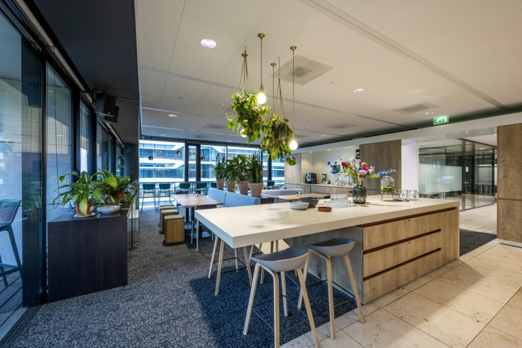 Modern office kitchen and lounge area on Gustav Mahlerlaan with wooden accents, indoor plants, and natural lighting.